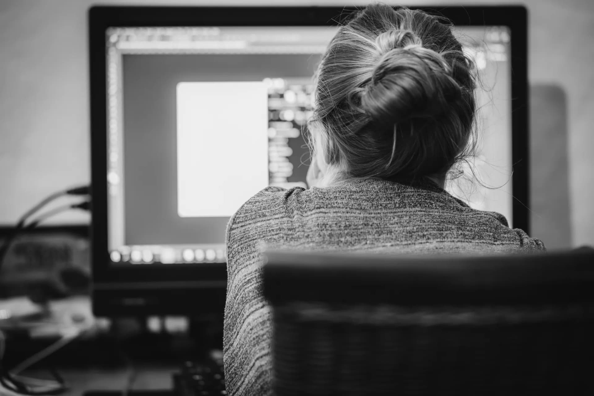 Black and white photograph of an editor working at a desktop monitor.