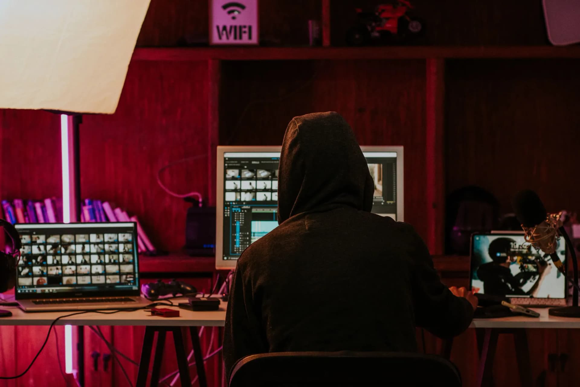 An editor in a hood works across several monitors in a red-lit edit suite.