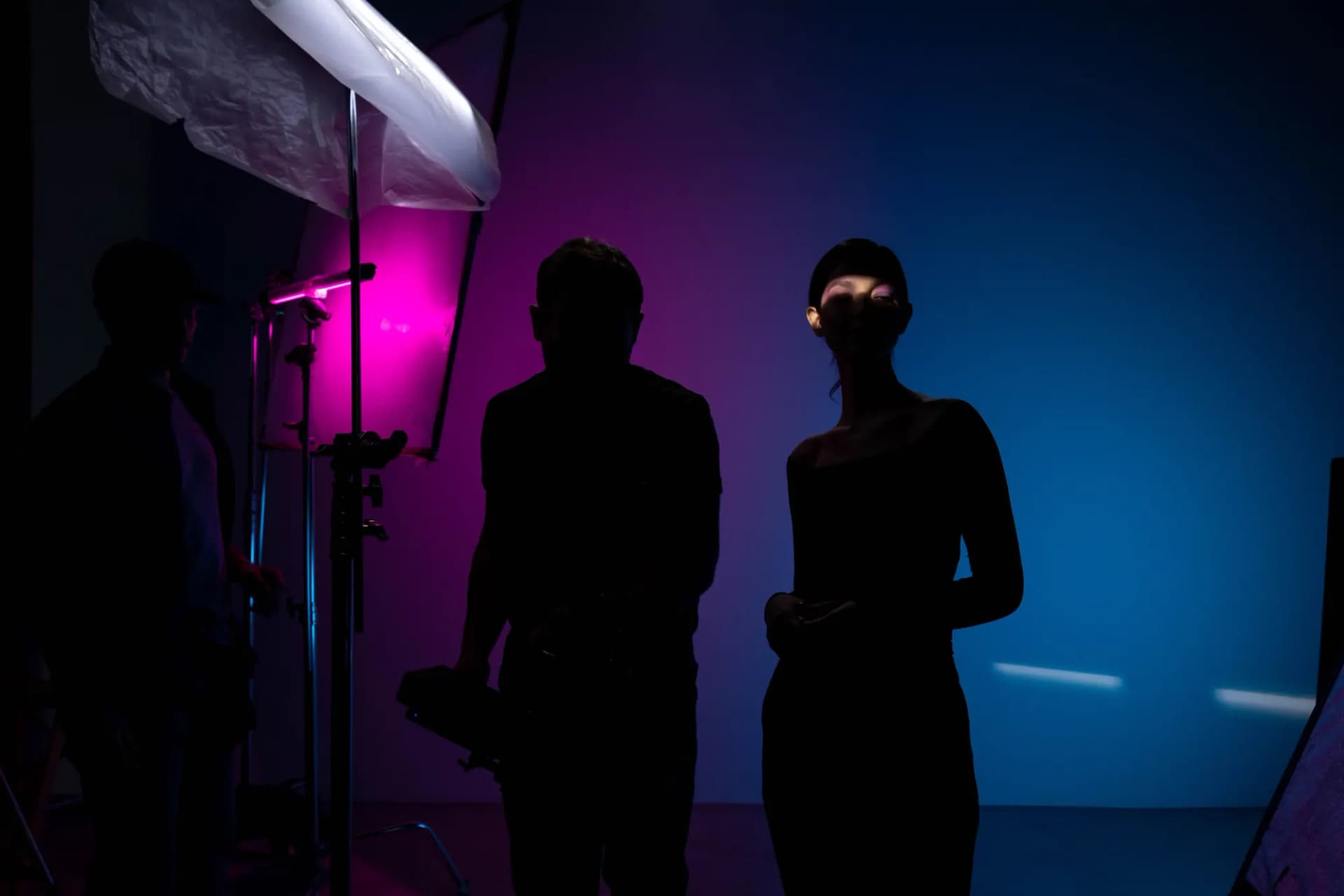 Silhouettes of a small crew on a set lit in magenta and blue.